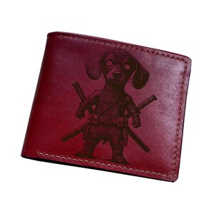Puede incluir: Cartera de cuero burdeos con un diseño de perro salchicha superhéroe grabado en el cuero. El perro está representado con dos espadas. La cartera tiene un borde cosido.