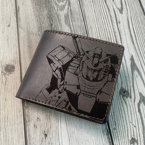 May include: A brown leather wallet with a black and white graphic of a robot. The robot has a large head with a visor and a large body with arms and legs.