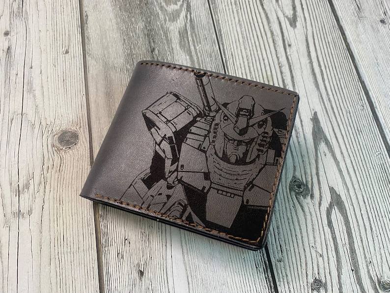 May include: A brown leather wallet with a black and white graphic of a robot. The robot has a large head with a visor and a large body with arms and legs.