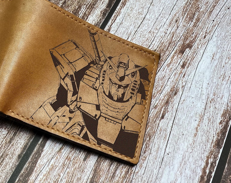 May include: A brown leather wallet with a laser-engraved image of a robot. The robot is in a dark brown color and has a detailed design.