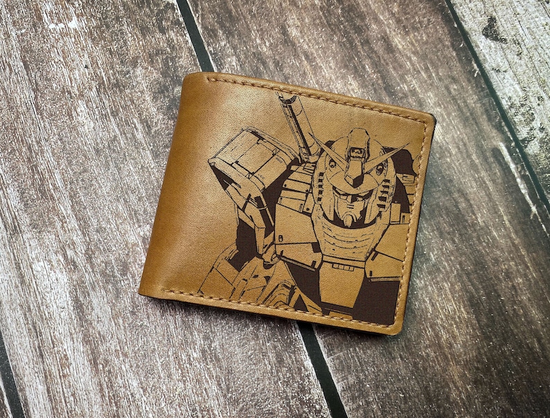 May include: A brown leather wallet with a laser-engraved image of a robot with a large head and a sword. The robot is in black and white.