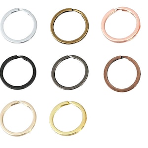 Könnte beinhalten: Sortiment von 10 Schlüsselringen in verschiedenen Ausführungen, darunter Silber, Gold, Bronze, Schwarz und Gunmetal.