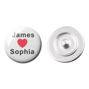 Puede incluir: Botón blanco con texto negro que dice "James ♥ Sophia". El corazón es rojo. El botón tiene una parte posterior plateada.