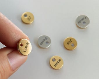 May include: Six small round metal tags with words engraved on them. The words are "Love", "Peace", "Joy", "Hope", "Family", and "07". The tags are gold and silver.