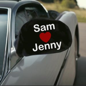May include: Black car mirror cover with the text "Sam ♥ Jenny" in white lettering and a red heart.