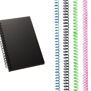 Pode incluir: Caderno preto de espiral com capa preta. O caderno está ao lado de um conjunto de seis espiras de encadernação de metal de diferentes cores. As cores são azul, preto, verde, rosa e laranja.