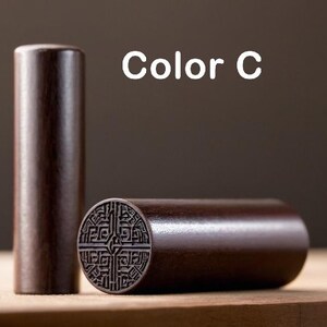 Peut inclure: Un tampon en bois brun fonc&eacute; avec un motif sculpt&eacute;. Le tampon est en forme de cylindre et a un dessus rond. Le tampon est sur une surface en bois. Couleur C.