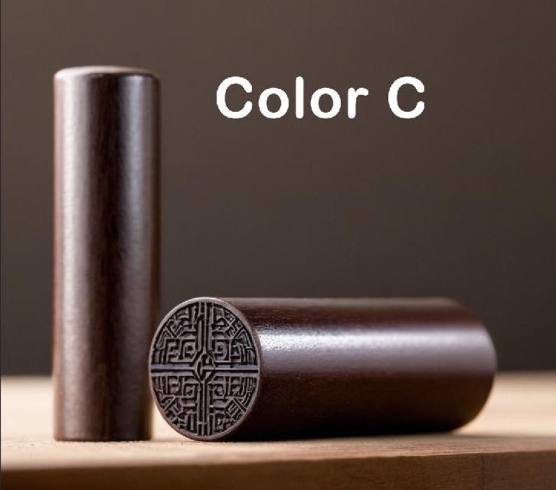 Peut inclure: Un tampon en bois brun fonc&eacute; avec un motif sculpt&eacute;. Le tampon est en forme de cylindre et a un dessus rond. Le tampon est sur une surface en bois. Couleur C.