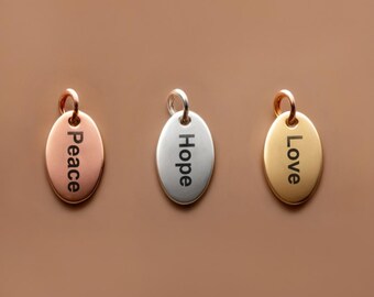 May include: Three oval-shaped metal charms with different words engraved on them. The charms are in rose gold, silver, and gold. The words are "Peace", "Hope", and "Love".