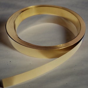 Può includere: Una striscia di rivestimento in metallo dorato, arrotolata in un cerchio e poi appiattita. La striscia è larga circa 2,5 cm.