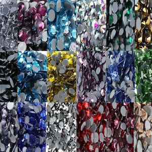 May include: Assortment of rhinestones in various colours, including clear, black, blue, green, red, gold, silver, and purple. The rhinestones are arranged in a grid pattern and are all the same size.