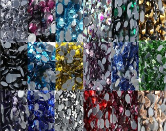 Könnte beinhalten: Sortiment an Strasssteinen in verschiedenen Farben, darunter klar, schwarz, blau, grün, rot, gold, silber und lila. Die Strasssteine sind in einem Rastermuster angeordnet und alle gleich groß.