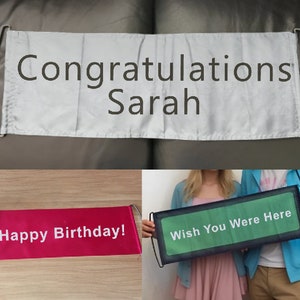 May include: Three retractable banners with different messages. The first banner is white with black text that reads "Congratulations Sarah". The second banner is red with white text that reads "Happy Birthday!". The third banner is green with white text that reads "Wish You Were Here".