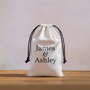 May include: A white drawstring bag with black drawstrings and the text "James & Ashley" printed on the front.