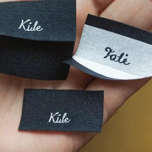 May include: Three black fabric labels with white text. The labels read "Kile" and "Falie".