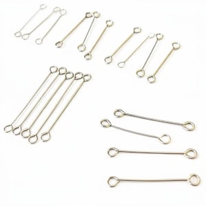 Op de afbeelding: Een verzameling zilverkleurige sieradenonderdelen, waaronder oogstiften en kopspelden, gerangschikt op een witte ondergrond. De onderdelen hebben aan elk uiteinde een lus en worden gebruikt voor het maken van sieraden en knutselen.