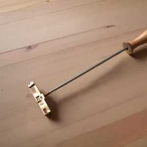 Puede incluir: Un hierro de marcar de latón con mango de madera. El hierro de marcar tiene forma rectangular y lleva las letras "ZFP" grabadas.