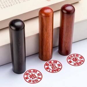 Peut inclure: Trois tampons en bois avec des impressions d'encre rouge. Les tampons sont cylindriques et ont un sommet arrondi. Les impressions d'encre sont circulaires et contiennent des caract&egrave;res chinois.