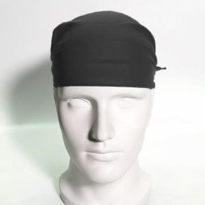 May include: A black surgical scrub cap made of a soft, smooth fabric. The cap is tied at the back with a thin black string.