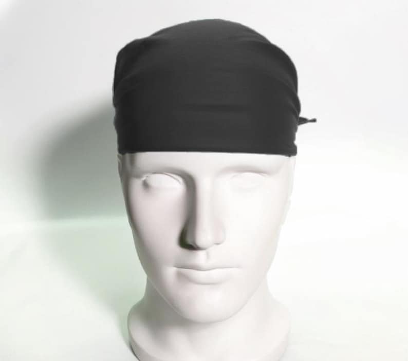 May include: A black surgical scrub cap made of a soft, smooth fabric. The cap is tied at the back with a thin black string.