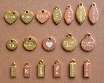 May include: Assortment of gold, rose gold, and silver charm pendants with various words and designs, including "Love", "Hope", "Peace", "Joy", "Unity", "Strength", "Patience", "Made by Jane", "Sam & Jes", "Created by Emy", "Family", "Mom", "Courage", "By Nina", "2025", and "N".