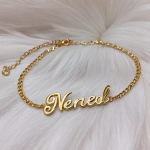 Peut inclure: Un bracelet en chaîne dorée avec le nom "Nene" écrit en cursive.