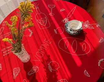 May include: Red round tablecloth with white embroidered designs of lemons, carrots, wine bottles, bread, and the word "VOMME".