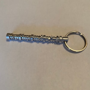 May include: A silver metal keychain shaped like a camshaft with a silver metal key ring.