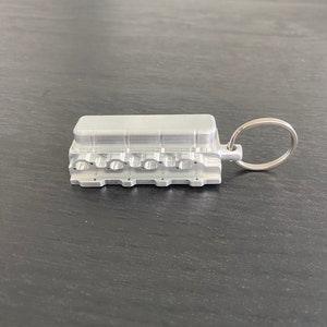 May include: A silver metal keychain shaped like an engine block. The keychain has a ring attached to it.