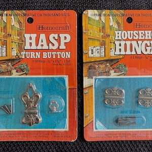 May include: Two vintage Homecraft hardware packages. One is a hasp and turn button set, the other is a set of household hinges. Both are on orange and blue packaging with decorative metal hardware.