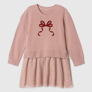 May include: A pale pink dress with long sleeves and a round neckline. The top is knitted, adorned with a red bow. The skirt is made of a sheer, dotted fabric. A stylish and comfortable outfit for any occasion.