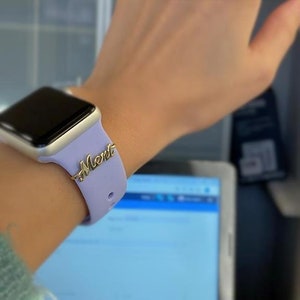 May include: A purple silicone watch band with a gold nameplate that says "Mert" on it.