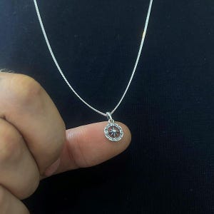 May include: A silver chain necklace with a small, round pendant featuring a starburst design.
