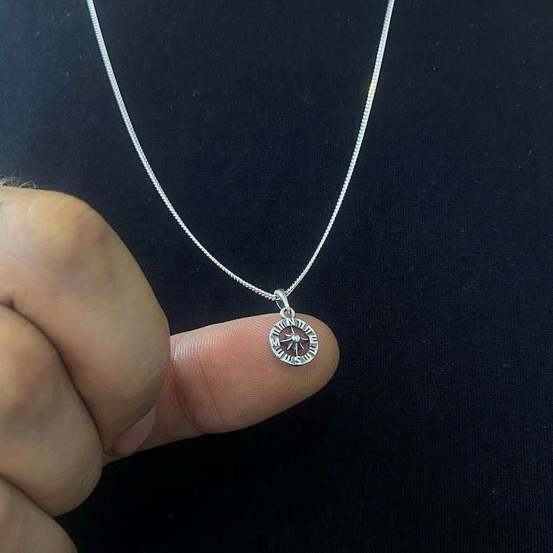 May include: A silver chain necklace with a small, round pendant featuring a starburst design.