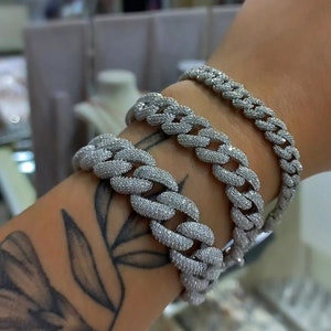 May include: Three silver chain bracelets with a diamond-like finish. The bracelets are stacked on a person's wrist.