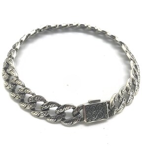 May include: A silver chain bracelet with a detailed, ornate design. The bracelet has a clasp closure.