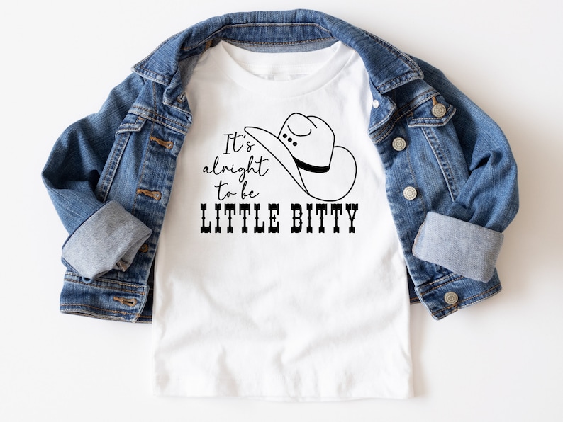 May include: White t-shirt with a black graphic of a cowboy hat and the text "It's alright to be LITTLE BITTY".