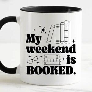 May include: White coffee mug with a black handle and black rim. The mug has a black graphic that says "My weekend is booked." with a stack of books and a pair of glasses.