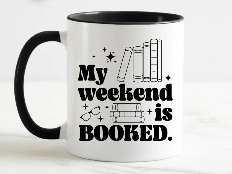 May include: White coffee mug with a black handle and black rim. The mug has a black graphic that says "My weekend is booked." with a stack of books and a pair of glasses.