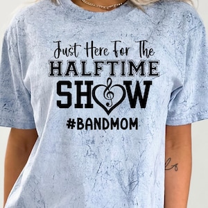 May include: Light blue tie-dye t-shirt with the text "Just Here For The Halftime Show" in black. A musical note heart design is between "Show" and "Halftime". The hashtag "#BANDMOM" is below the text.