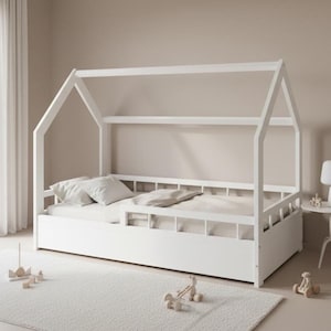 Può includere: Un letto in legno bianco a forma di casa con un profilo basso. Il letto ha una testiera e una pediera a doghe e una struttura a baldacchino. Il letto è su un tappeto bianco e ci sono cuscini e un piumino sul letto.