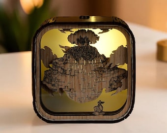 May include: A square wooden night light with a detailed, layered design depicting a mountain scene with a tree and a figure. The interior glows with a warm, golden light, creating a cozy ambiance. The wood has a natural grain.