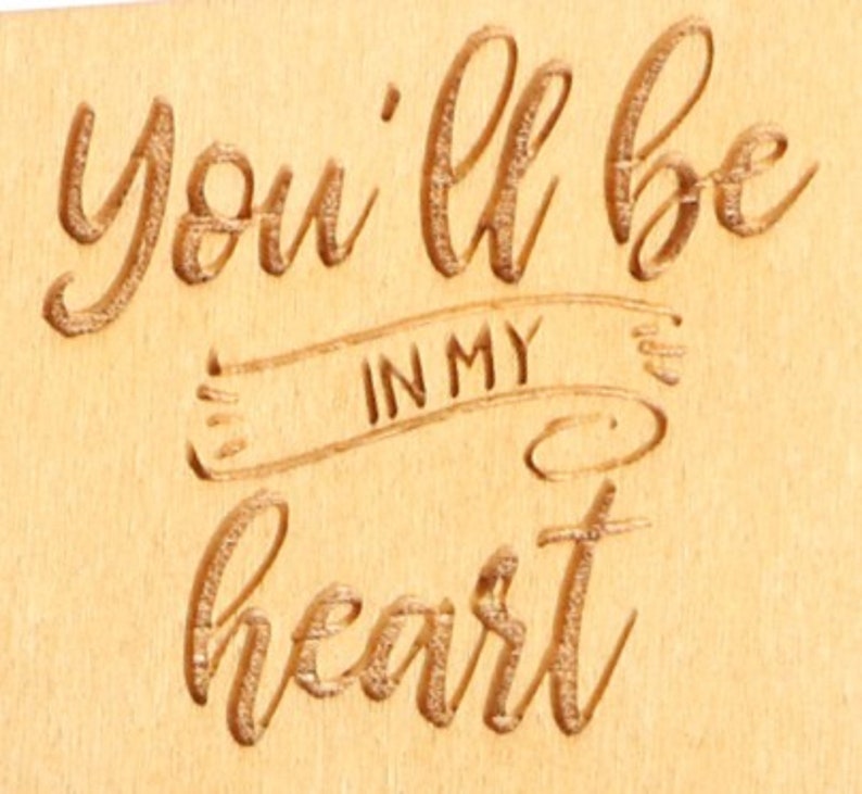 May include: A wooden plaque with the engraved phrase "You'll be in my heart." The text is in a flowing script and is centered on the light-colored wood. The words "IN MY" are within a banner design.