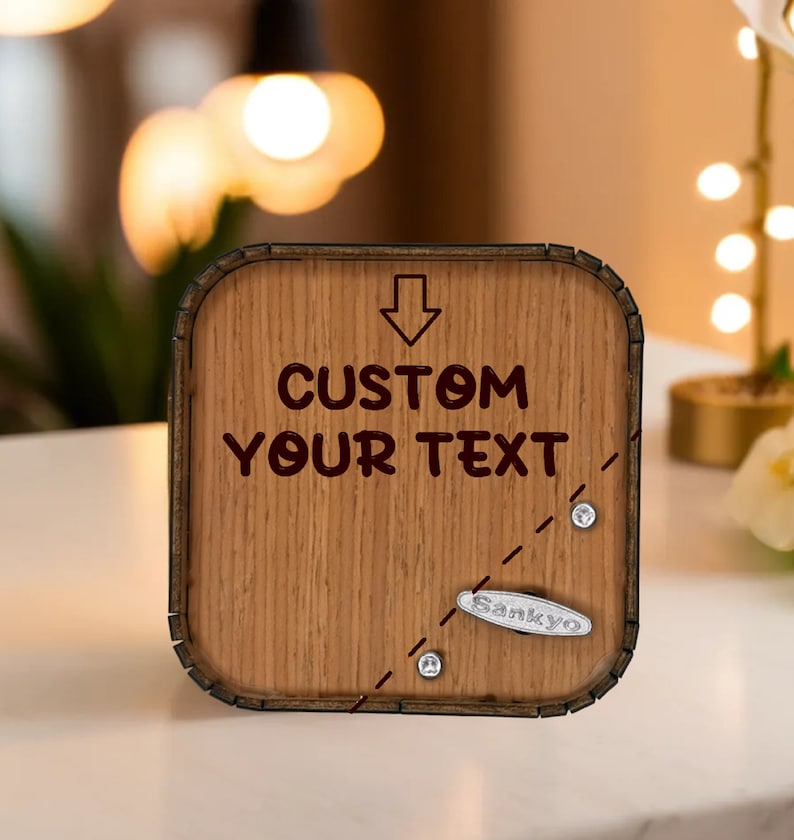 May include: Wooden music box with the text "CUSTOM YOUR TEXT" and an arrow pointing down. The box has a light brown wood grain finish, a Sankyo music mechanism, and decorative silver accents.