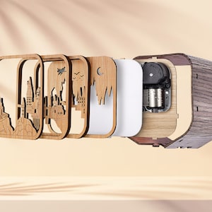 May include: A wooden music box with a layered design featuring a castle silhouette. The box has a dark wood grain exterior and a visible mechanical interior. The layered design includes a white panel and laser-cut wooden frames.