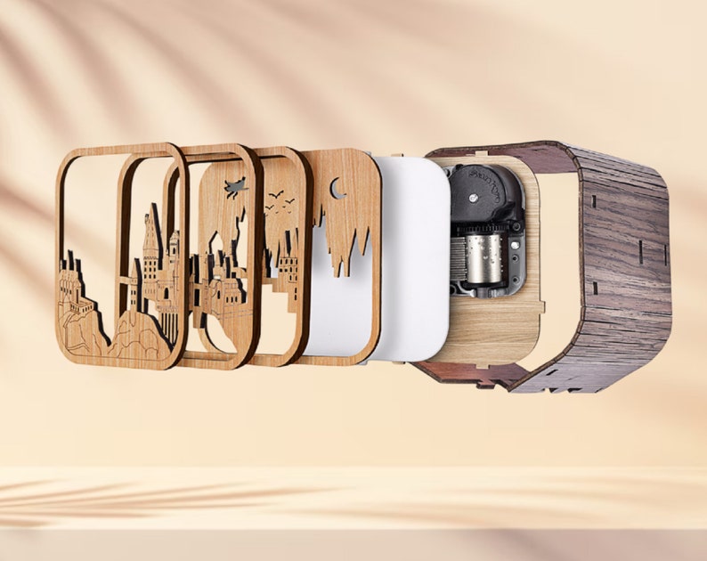 May include: A wooden music box with a layered design featuring a castle silhouette. The box has a dark wood grain exterior and a visible mechanical interior. The layered design includes a white panel and laser-cut wooden frames.