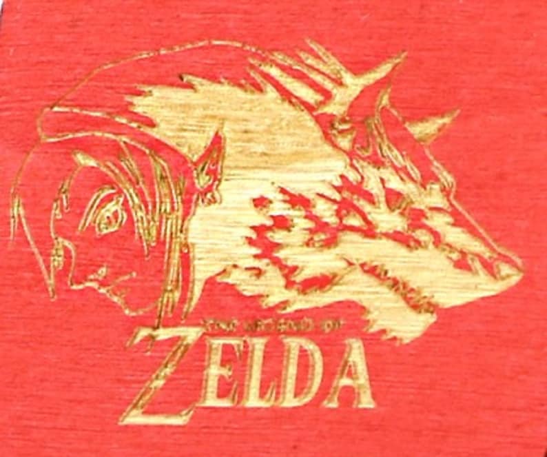 May include: A red wooden surface with a gold-colored engraved design featuring a profile of a person and a boar's head. The text "THE LEGEND OF ZELDA" is below the images.