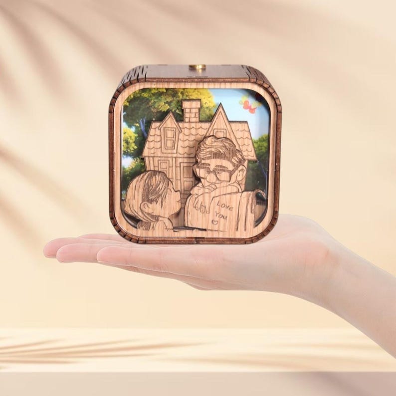 May include: A wooden music box with a carved design featuring a house and two figures kissing. The box has a light brown finish and a small, round knob on top. The words "Love You" are carved on the box.