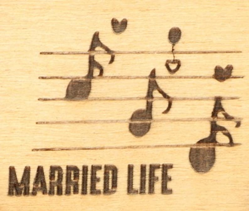 May include: A wooden plaque with engraved musical notes and hearts on a staff. The words "MARRIED LIFE" are etched below the staff. The background is a light wood grain.