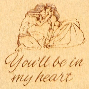 May include: A wooden plaque with an engraved romantic scene of a couple embracing. The text "You'll be in my heart" is elegantly carved below the image. The wood has a light, natural tone.